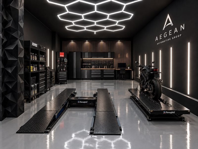 Το studio στα Χανιά: εξαγωνικό πλέγμα LED στην οροφή, κάθετες γραμμές φωτός στους ανθρακί τοίχους, γκρι epoxy δάπεδο, ανυψωτικά και πάγκος εργαλείων.